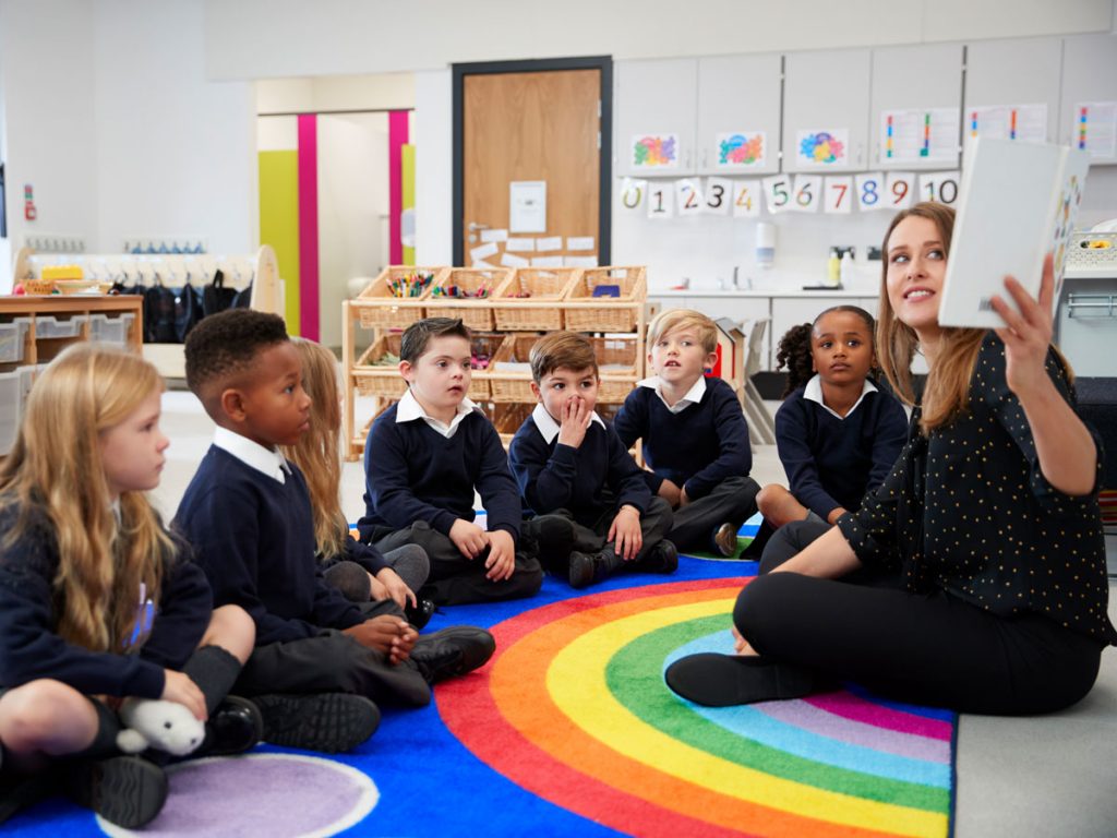 Teacher leading a class of students seated on a rainbow mat