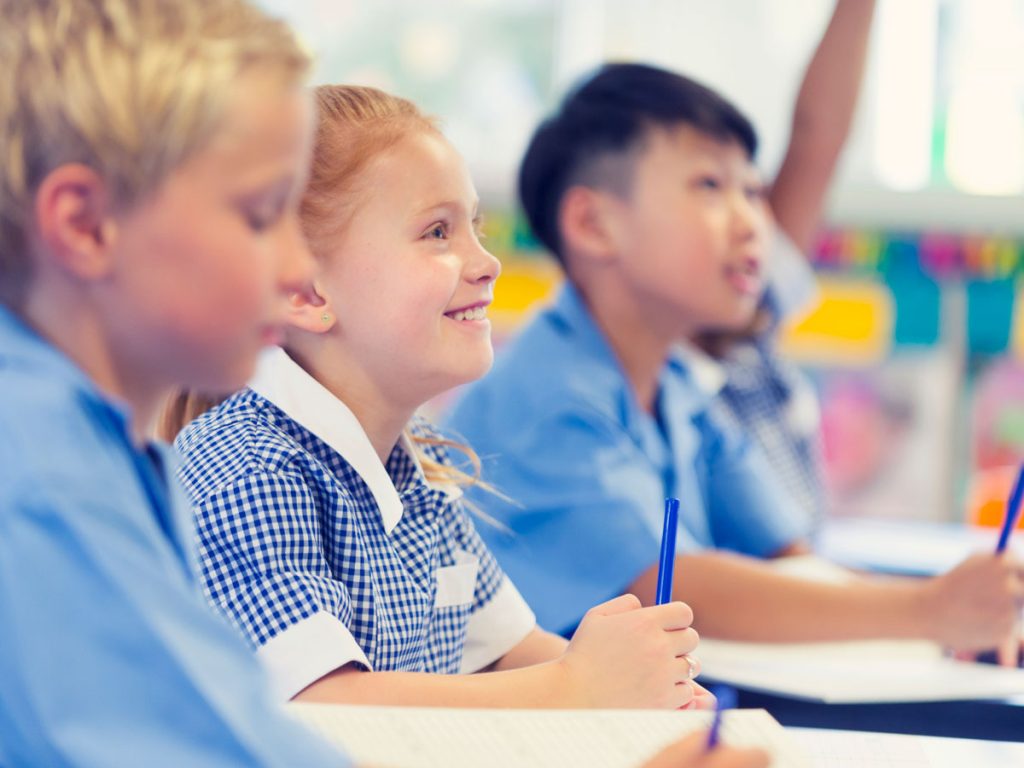 Primary school students smiling and writing at their desks